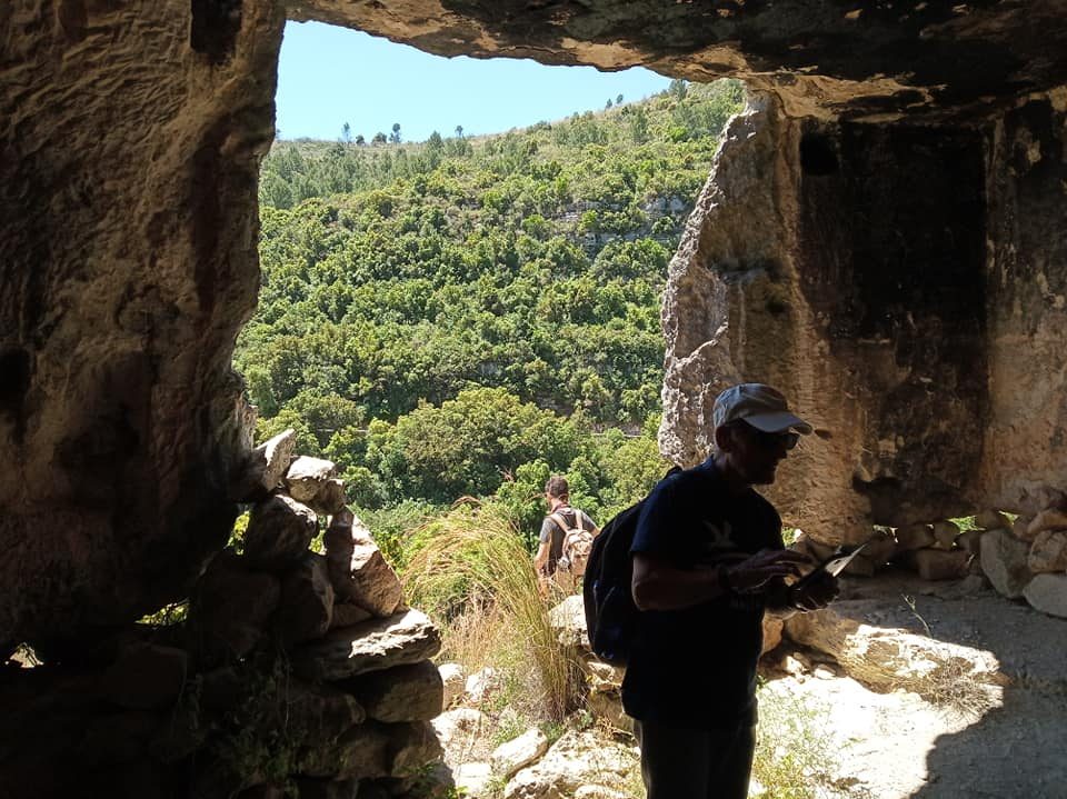 A walker looking out from a rock shelter over a green valley