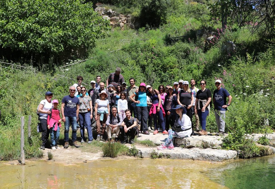 A large group on a BirdLife Malta nature walk posing beside a valley pool