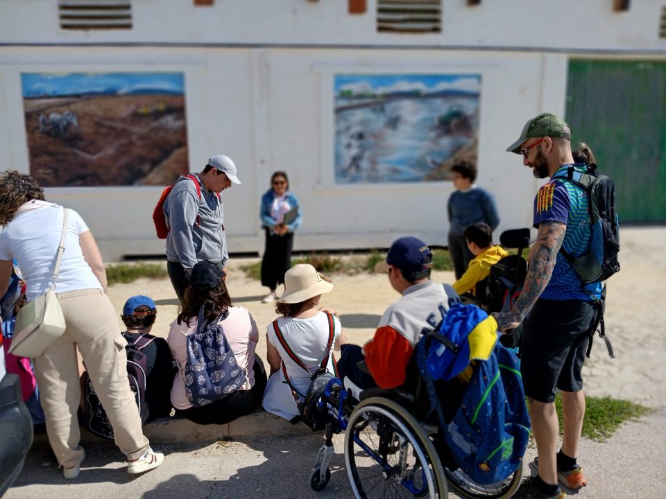 Grupo de visitantes, con personas en silla de ruedas y niños, sentados frente a un edificio de la reserva