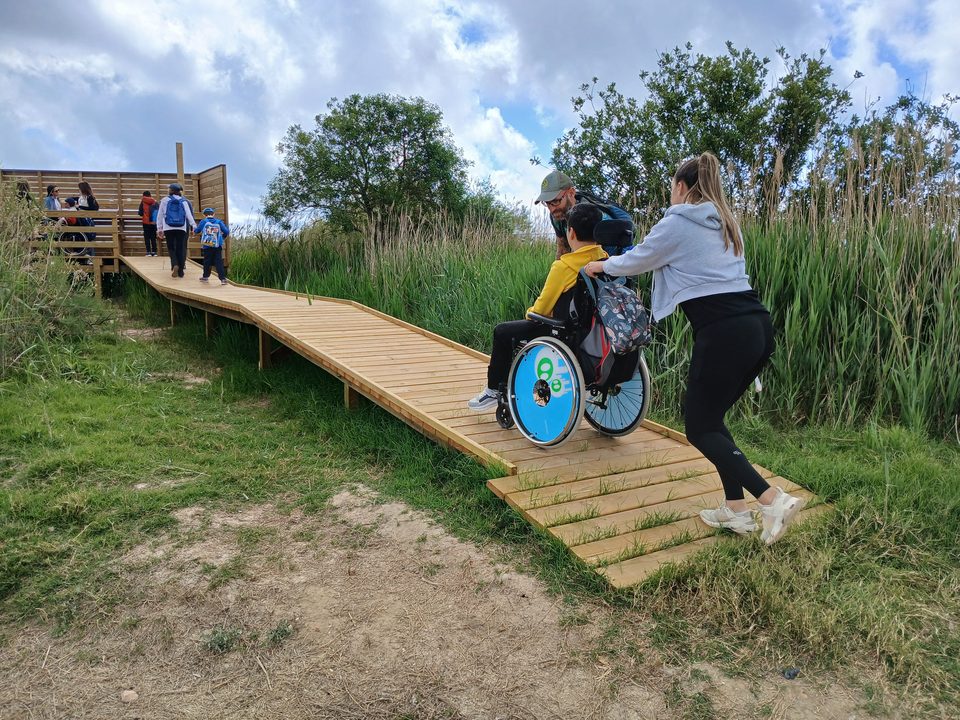 Una mujer empuja a un joven en silla de ruedas por la pasarela de madera accesible