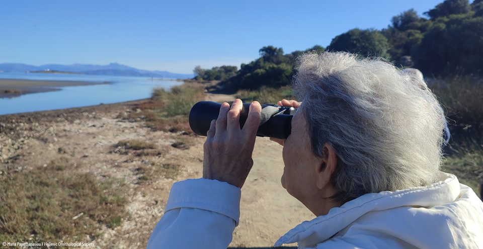Ηλικιωμένη γυναίκα παρατηρεί με κιάλια έναν παράκτιο υγρότοπο