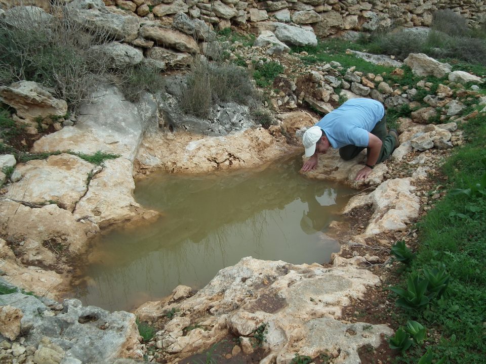 A worker bending over a small rocky water hole
