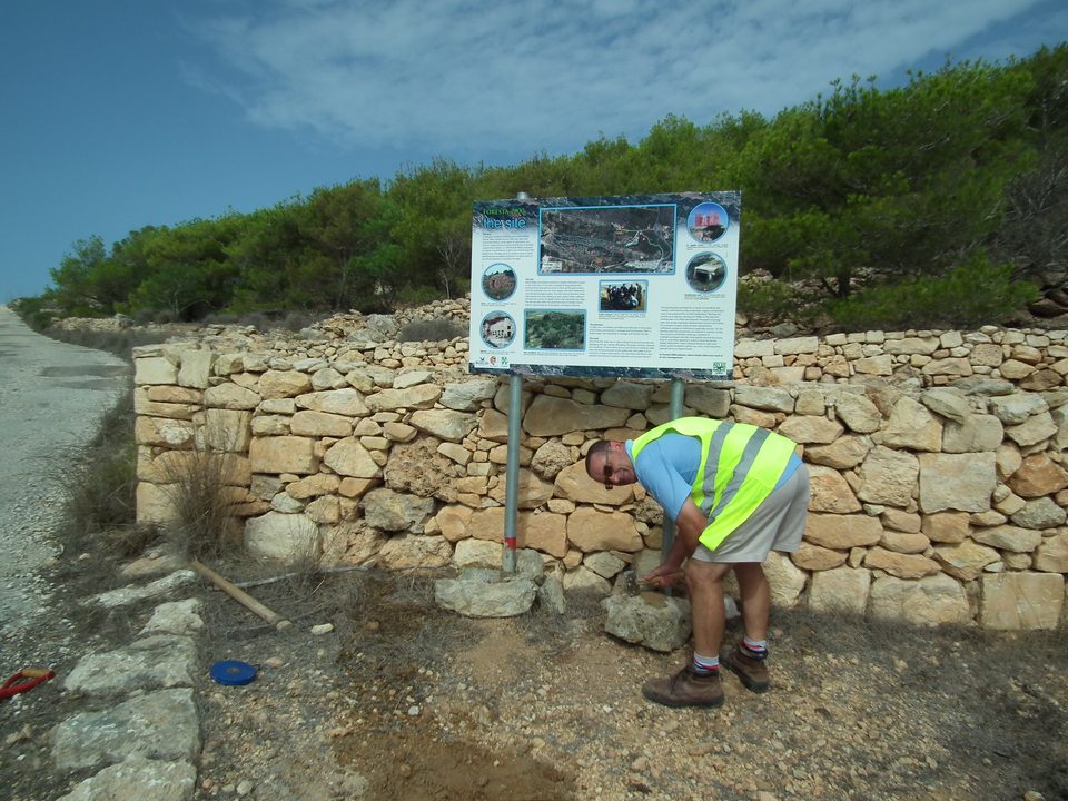 A worker fixing a new information sign in front of a rubble wall