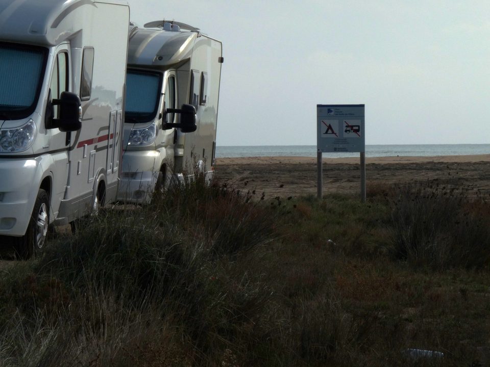 Autocaravanas aparcadas en la playa junto a una señal