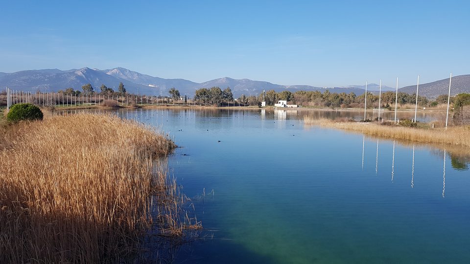 Γαλάζια λίμνη με καλαμιώνα και βουνά στο βάθος