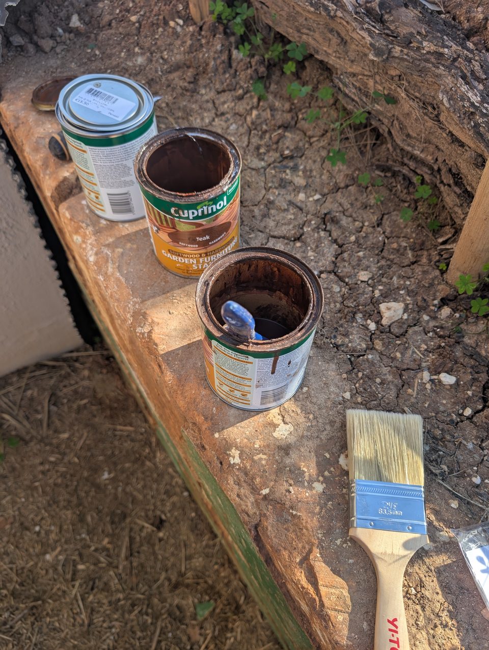 Tins of wood stain and a brush on a wooden rail