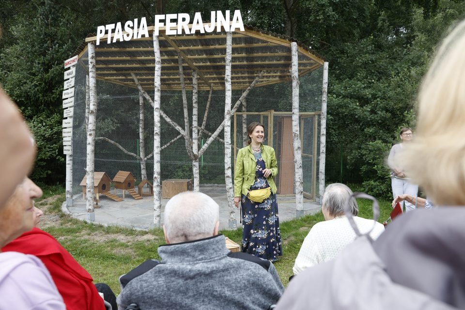 Ewa Rumińska przed nową wolierą z napisem „Ptasia Ferajna”, na pierwszym planie seniorzy widziani od tyłu