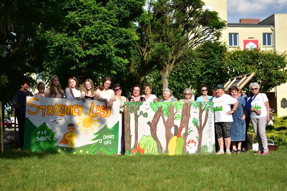 Uczestnicy projektu stoją za namalowanymi muralami „Strażnicy Lasu” na trawniku przed budynkiem
